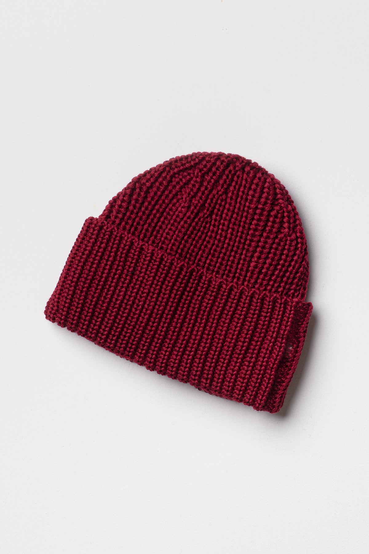Bonnet rouge rubis en laine mérinos à revers, packshot sur fond clair montrant la maille côtelée. Made in France.