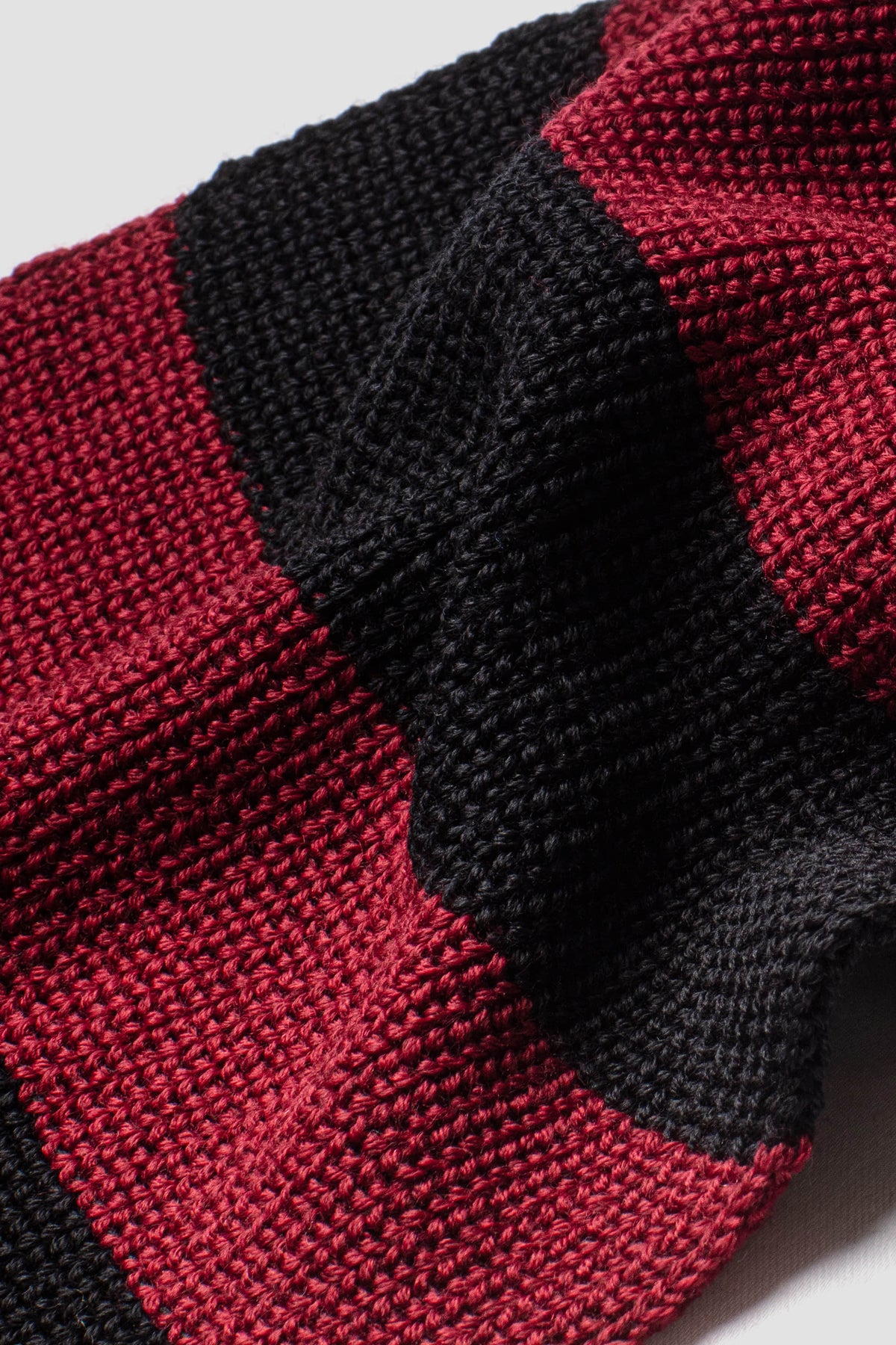 Écharpe rayée rouge rubis et noir en laine mérinos, gros plan sur la maille et la jonction des couleurs.