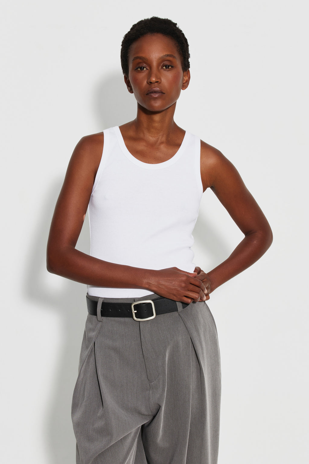 Débardeur Marcel Signature blanc femme, porté de face avec un pantalon gris, mains croisées à la taille.