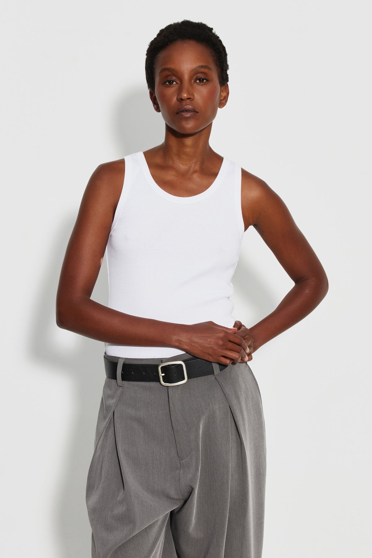 Débardeur Marcel Signature blanc femme, porté de face avec un pantalon gris, mains croisées à la taille.