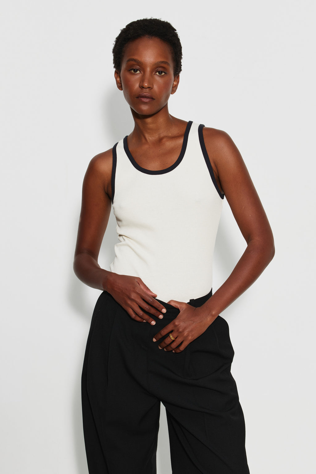 Débardeur femme écru et noir en coton Pima côtelé, porté de face avec un pantalon noir, les mains devant la taille. Made in France.