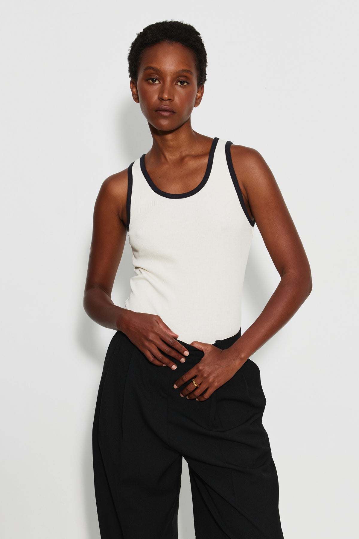 Débardeur femme écru et noir en coton Pima côtelé, porté de face avec un pantalon noir, les mains devant la taille. Made in France.