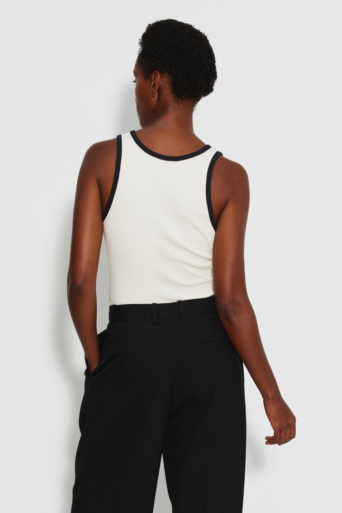 Débardeur femme écru et noir en coton Pima côtelé, porté de dos avec un pantalon noir.