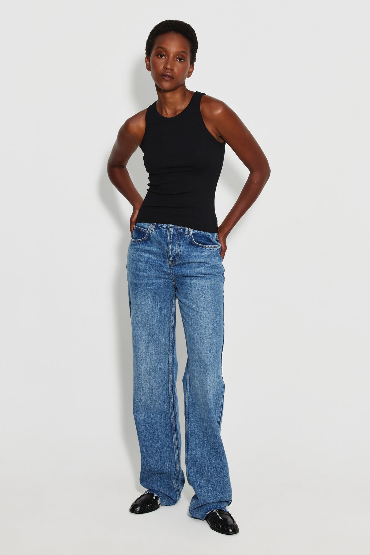 Débardeur Top Marcel noir femme, porté avec un jean large bleu et des chaussures noires, vue de face en pied.