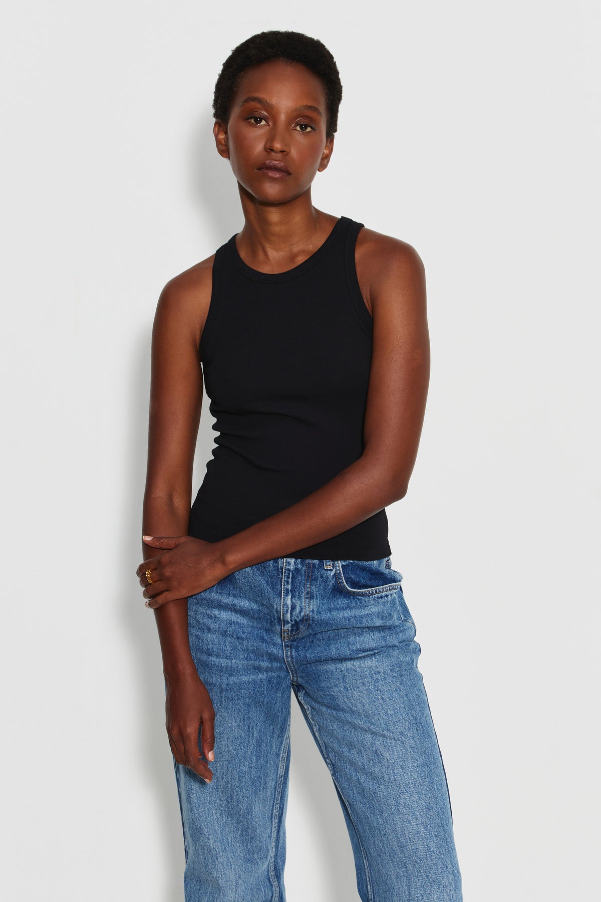 Débardeur Top Marcel noir femme en coton Pima et élasthanne, porté de face avec un jean bleu, les mains croisées devant le corps.