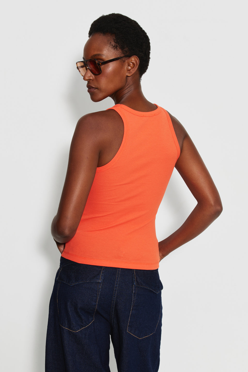 Débardeur Top Marcel orange femme en coton Pima et élasthanne, porté de dos avec un jean bleu foncé, une main sur la hanche.