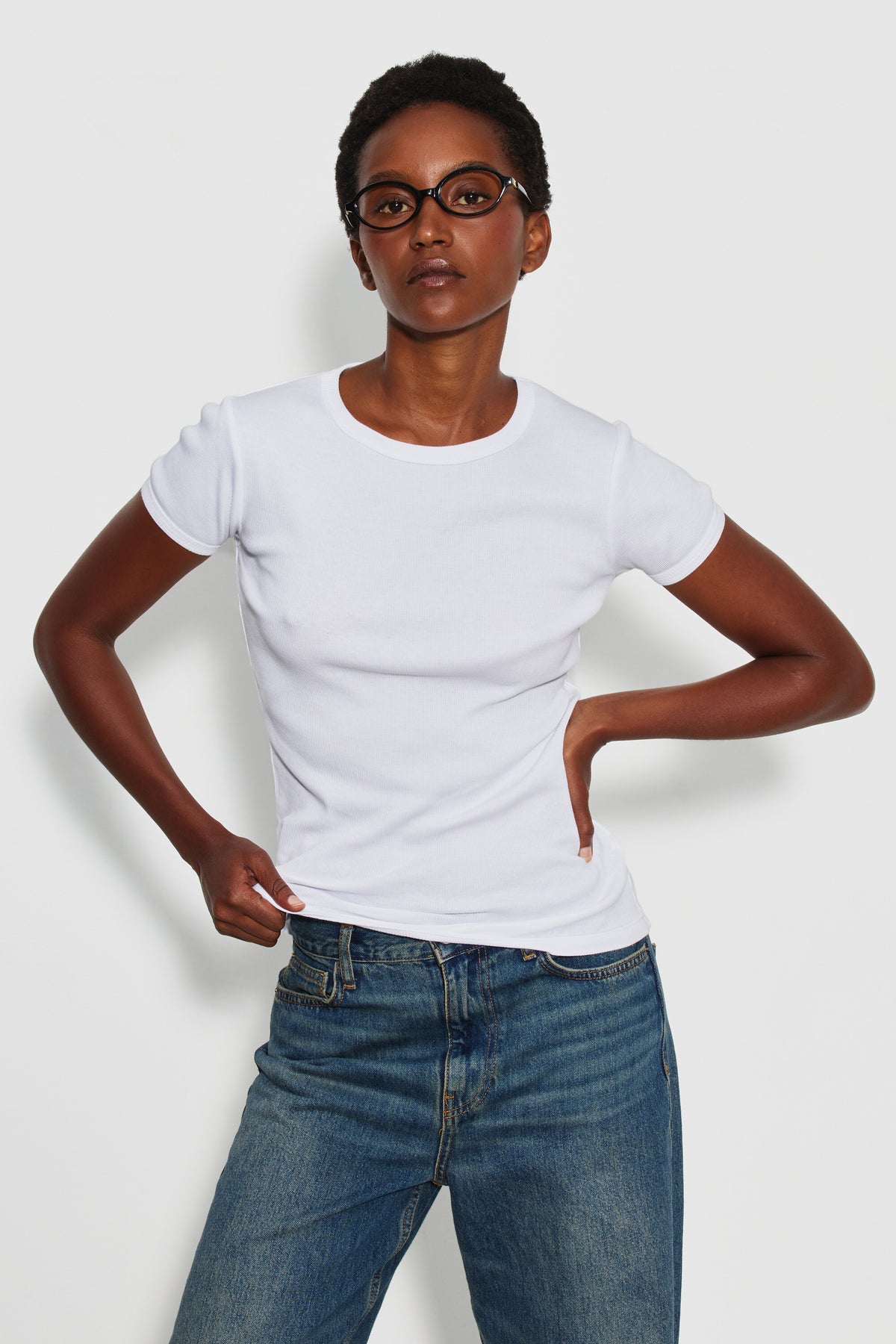 Maillot de corps femme blanc à manches courtes en coton Pima côtelé, porté de face avec un jean bleu, une main sur la hanche. Made in France.