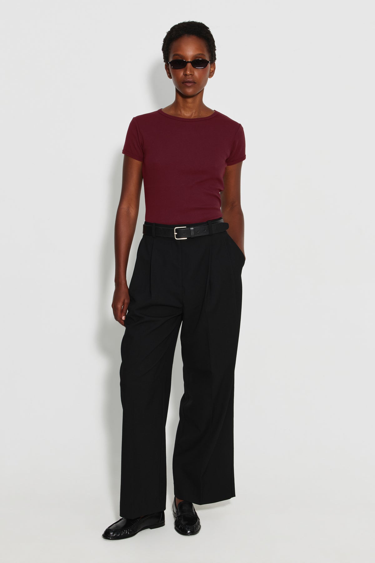 Maillot de corps femme bordeaux en coton pima côtelé à manches courtes, porté avec un pantalon noir et des lunettes de soleil, vue de face en pied.