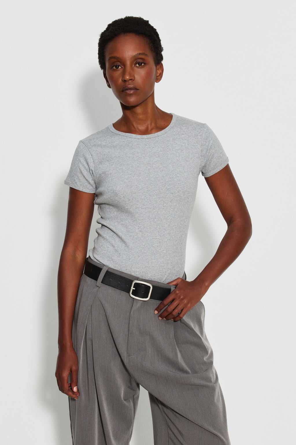 Maillot de corps femme gris chiné à manches courtes en coton Pima côtelé, porté de face avec un pantalon gris, une main près de la ceinture. Made in France.