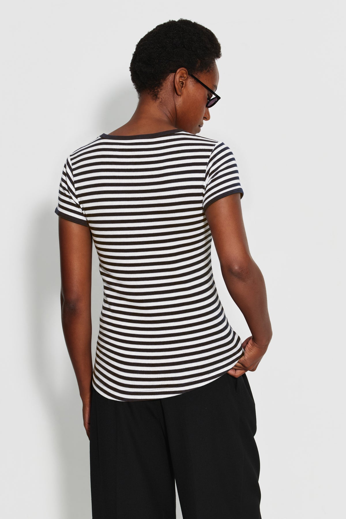 Maillot de corps femme noir et écru en coton bio côtelé à manches courtes, porté de dos avec un pantalon noir, vue des rayures et des manches.