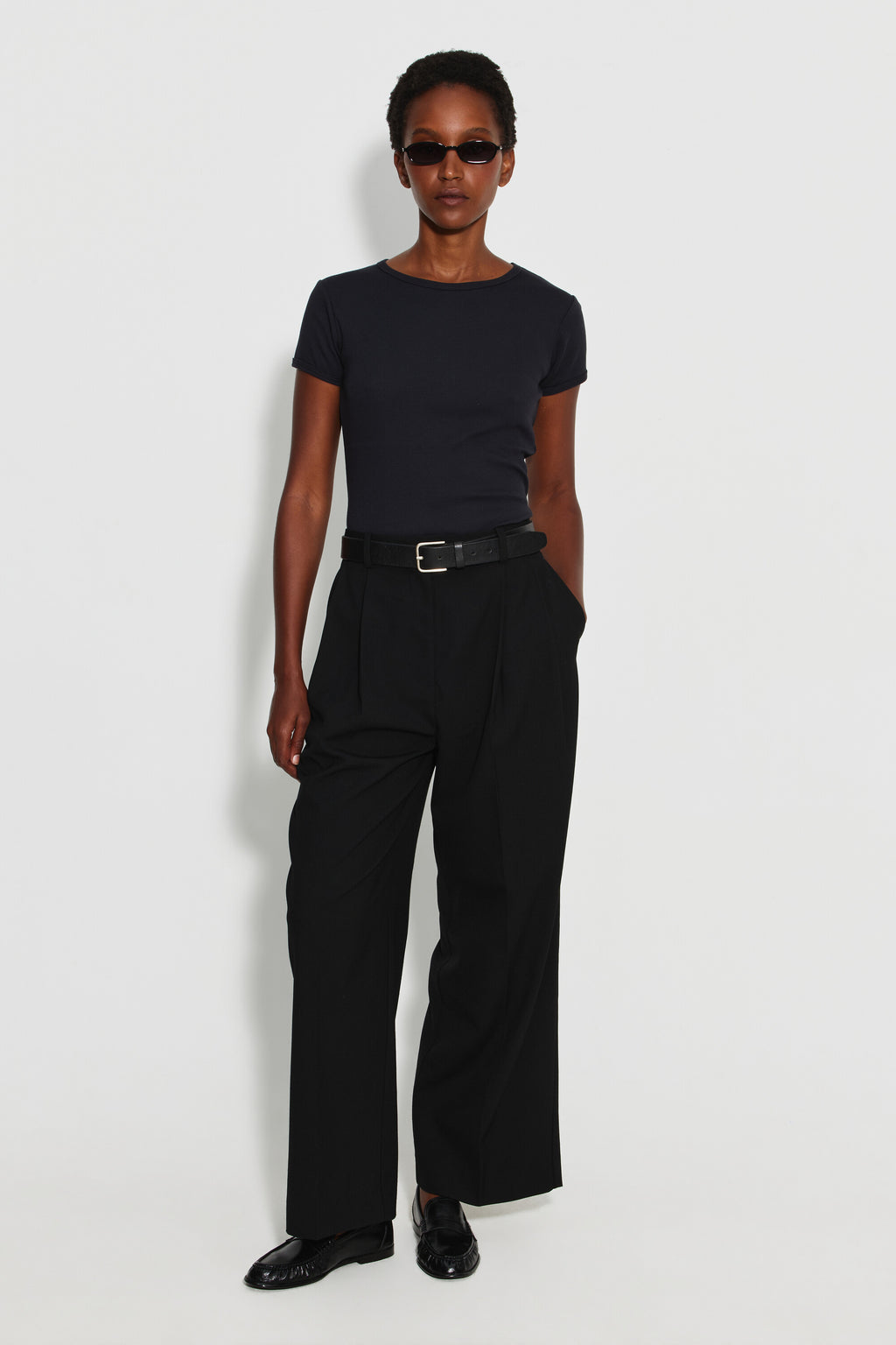 Maillot de corps femme noir à manches courtes en coton Pima côtelé, porté avec un pantalon noir et des lunettes de soleil, vue de face en pied.