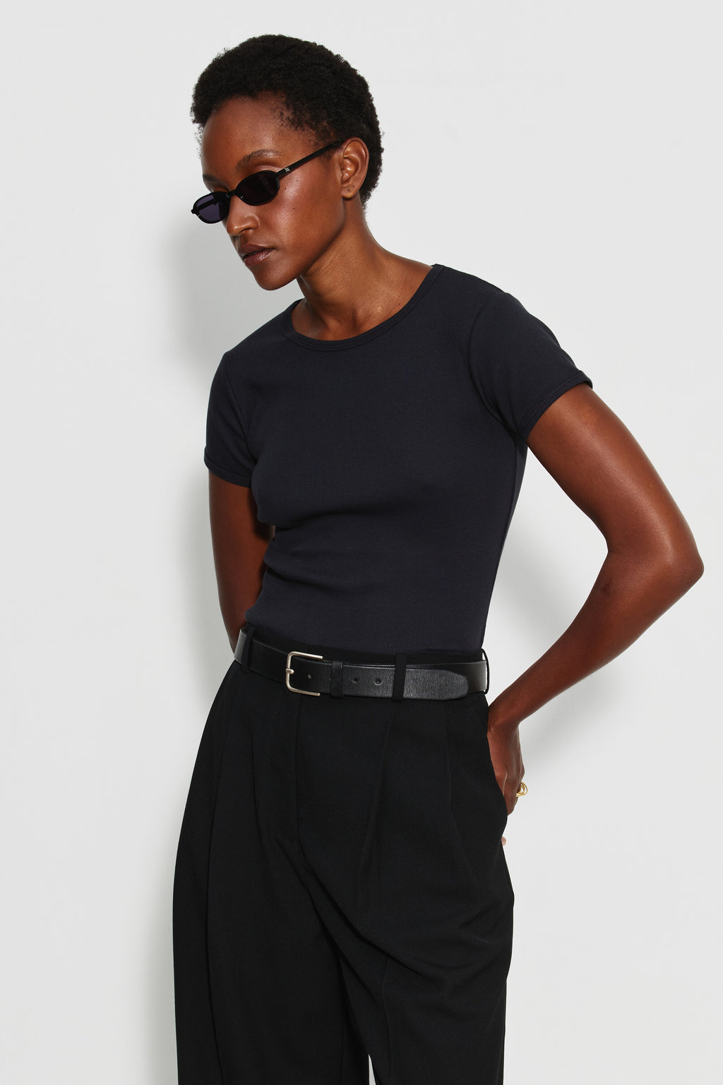 Maillot de corps femme noir à manches courtes en coton Pima côtelé, porté de trois quarts avec un pantalon noir, une main sur la hanche. Made in France.