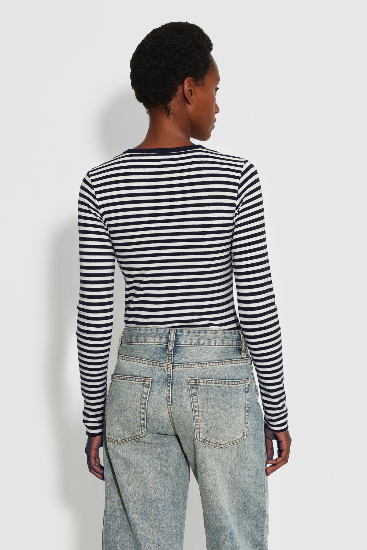 Maillot de corps femme bleu marine et écru en coton bio côtelé à manches longues, porté de dos avec un jean bleu clair, vue des rayures et des manches longues.