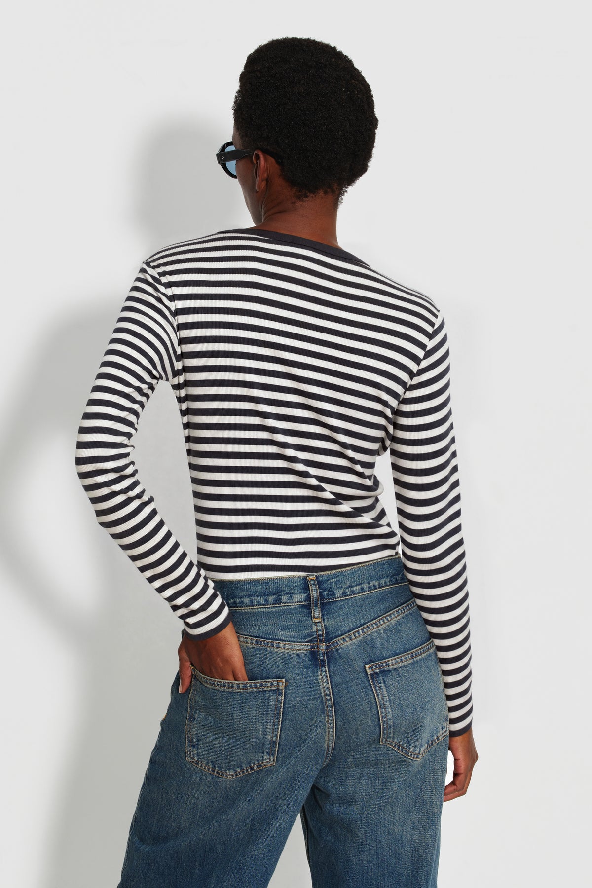 Maillot de corps femme noir et écru en coton bio côtelé à manches longues, porté de dos avec un jean bleu, vue des rayures et des manches longues.