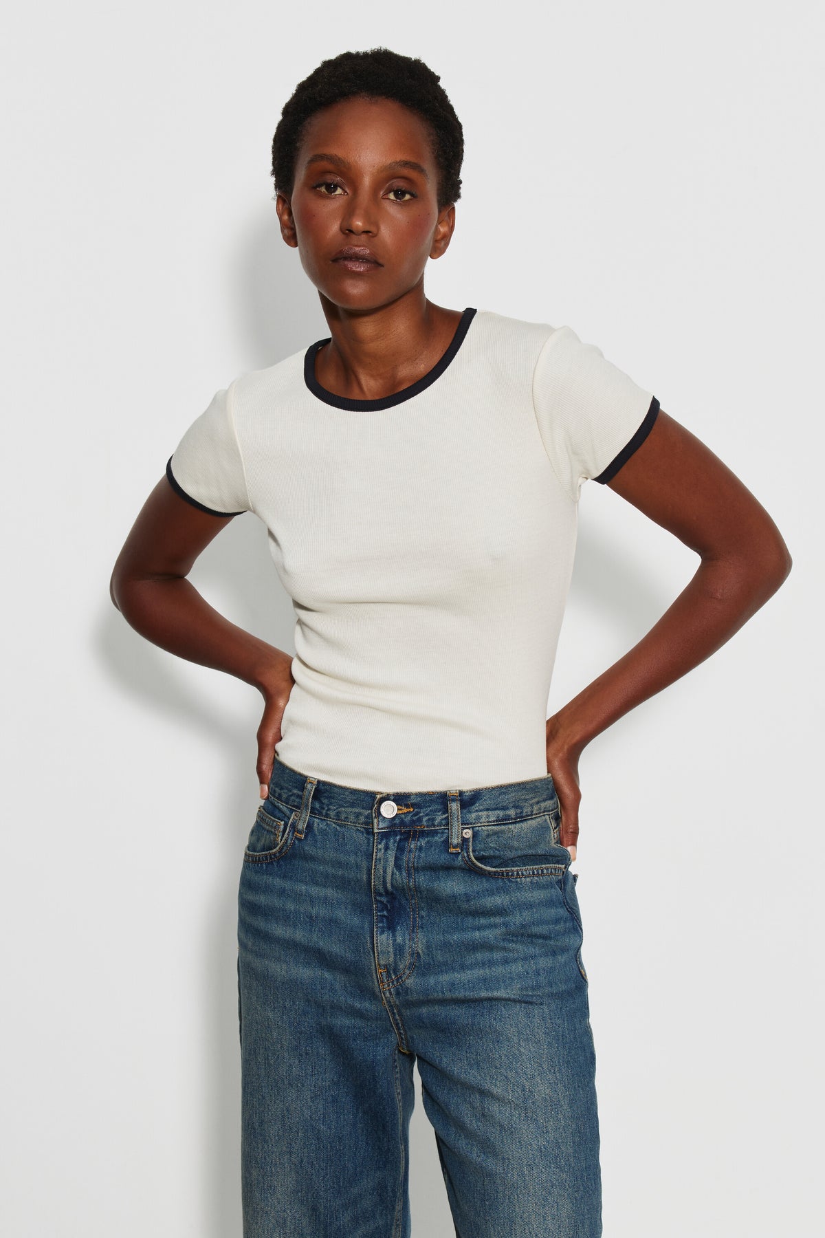 Maillot de corps femme bicolore écru et noir à manches courtes en coton Pima côtelé, porté de face avec un jean bleu, les mains sur les hanches. Made in France.