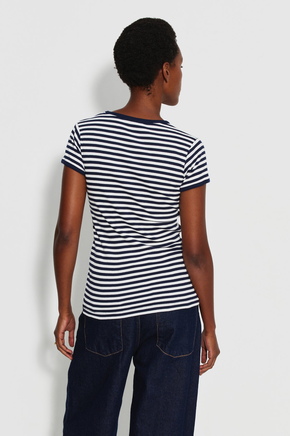 Maillot de corps femme bleu marine et écru en coton bio côtelé à manches courtes, porté de dos avec un jean bleu foncé, la tête tournée sur le côté.