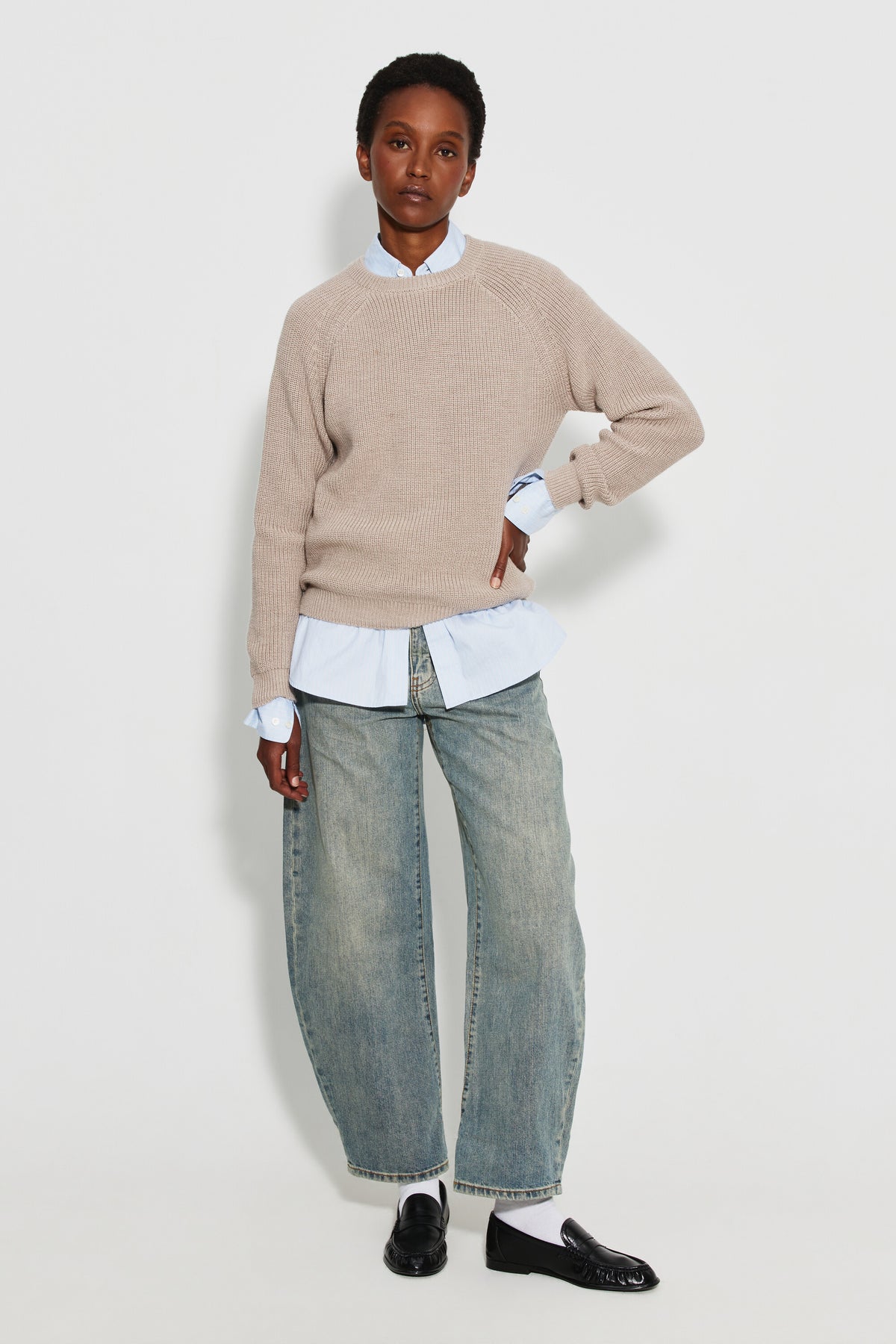 Pull femme beige en laine mérinos à manches raglan, porté sur une chemise bleu clair avec un jean clair et des chaussures noires, vue de face en pied.