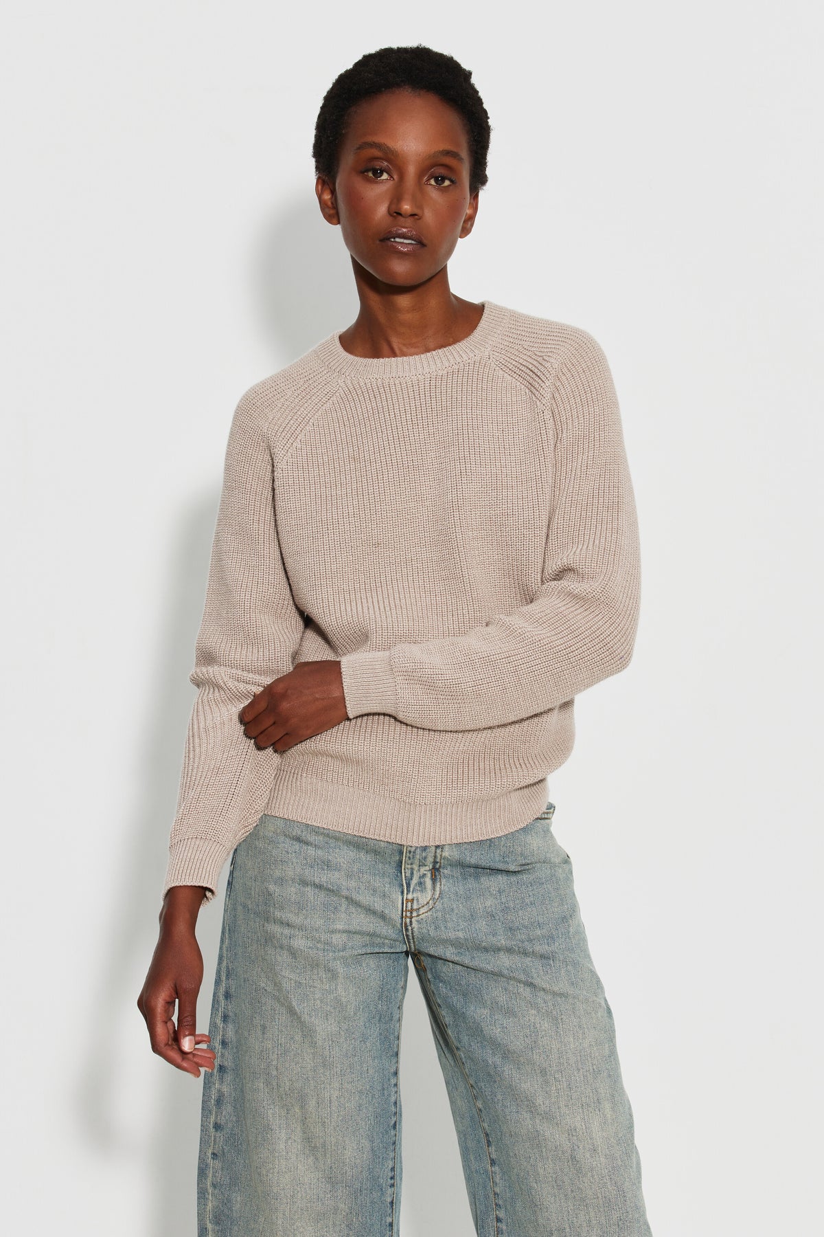 Pull femme beige en laine mérinos à manches raglan, porté de face avec un jean clair, une main sur l’avant-bras. Made in France.