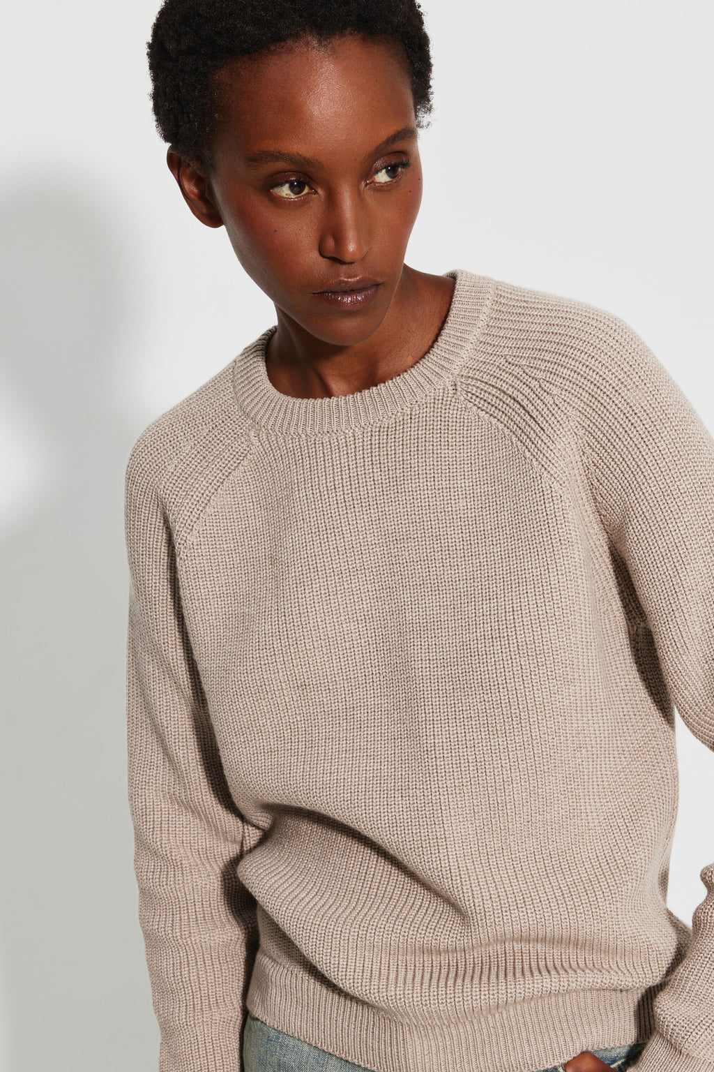 Pull femme beige en laine mérinos à manches raglan, portrait de trois quarts montrant le col rond, les manches raglan et la maille perlée.