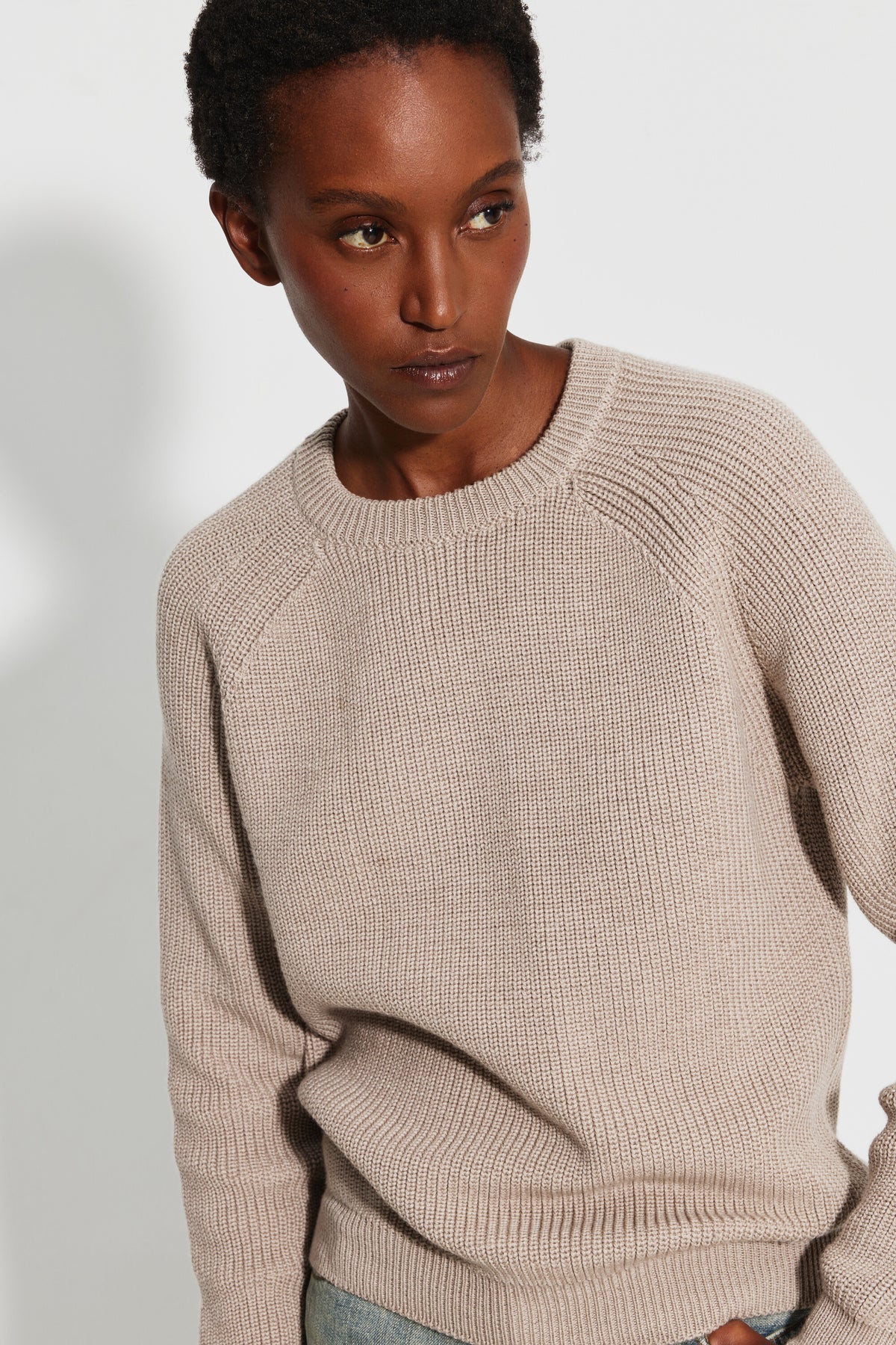 Pull femme beige en laine mérinos à manches raglan, portrait de trois quarts montrant le col rond, les manches raglan et la maille perlée.
