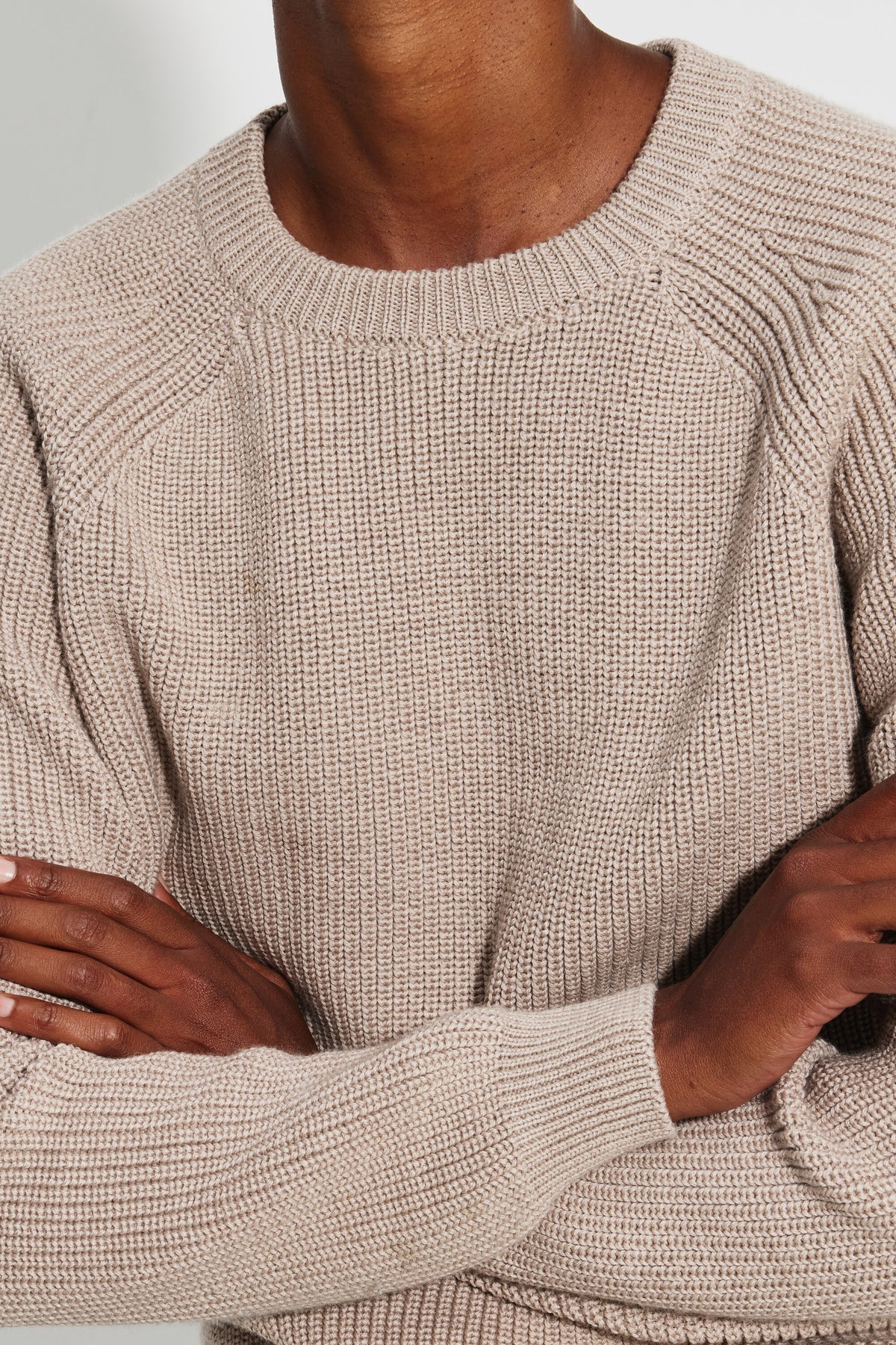 Pull femme beige en laine mérinos à manches raglan, gros plan du col rond, des manches raglan et des poignets côtelés, les bras croisés.