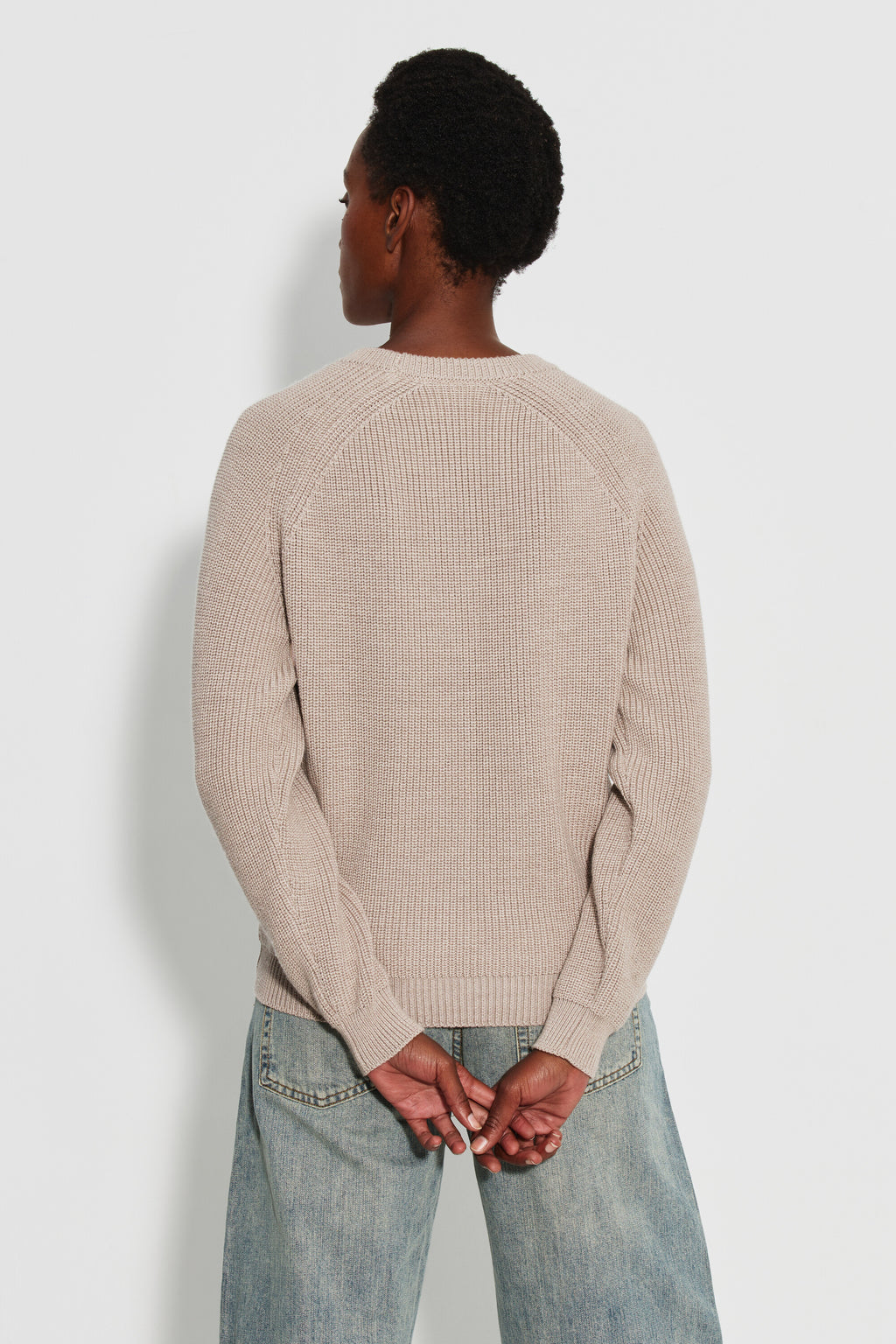 Pull femme beige en laine mérinos à manches raglan, porté de dos avec un jean clair, les mains derrière le dos.