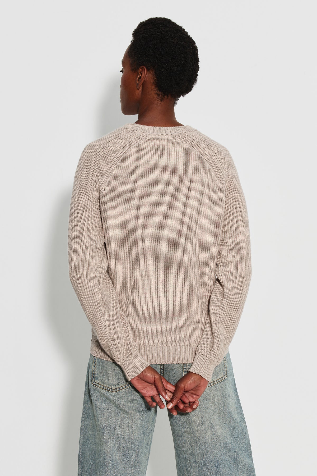Pull femme beige en laine mérinos à manches raglan, porté de dos avec un jean clair, les mains derrière le dos.