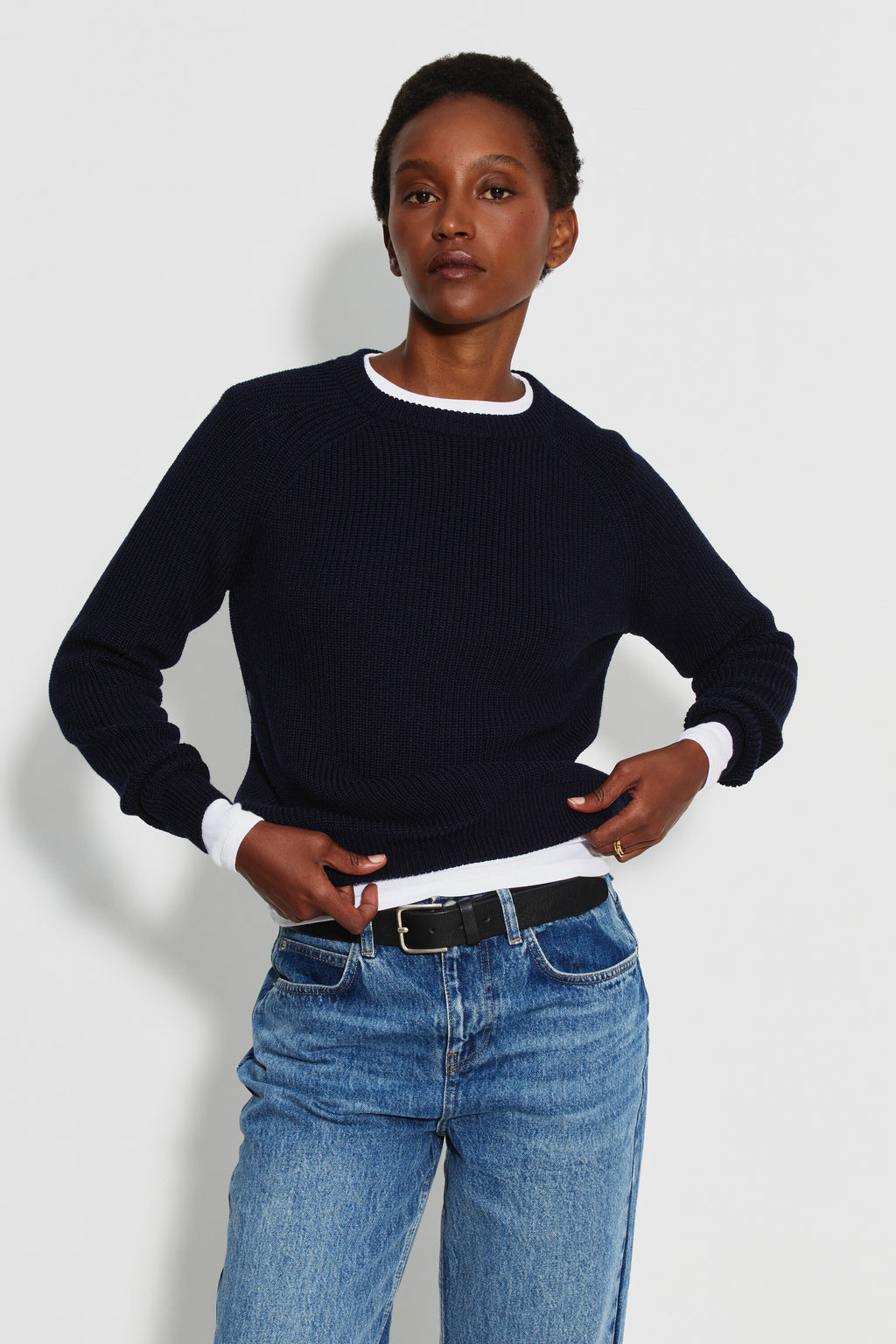 Pull femme bleu marine en laine mérinos à manches raglan, porté de face avec un jean bleu et une ceinture noire, les mains près de la taille. Made in France.