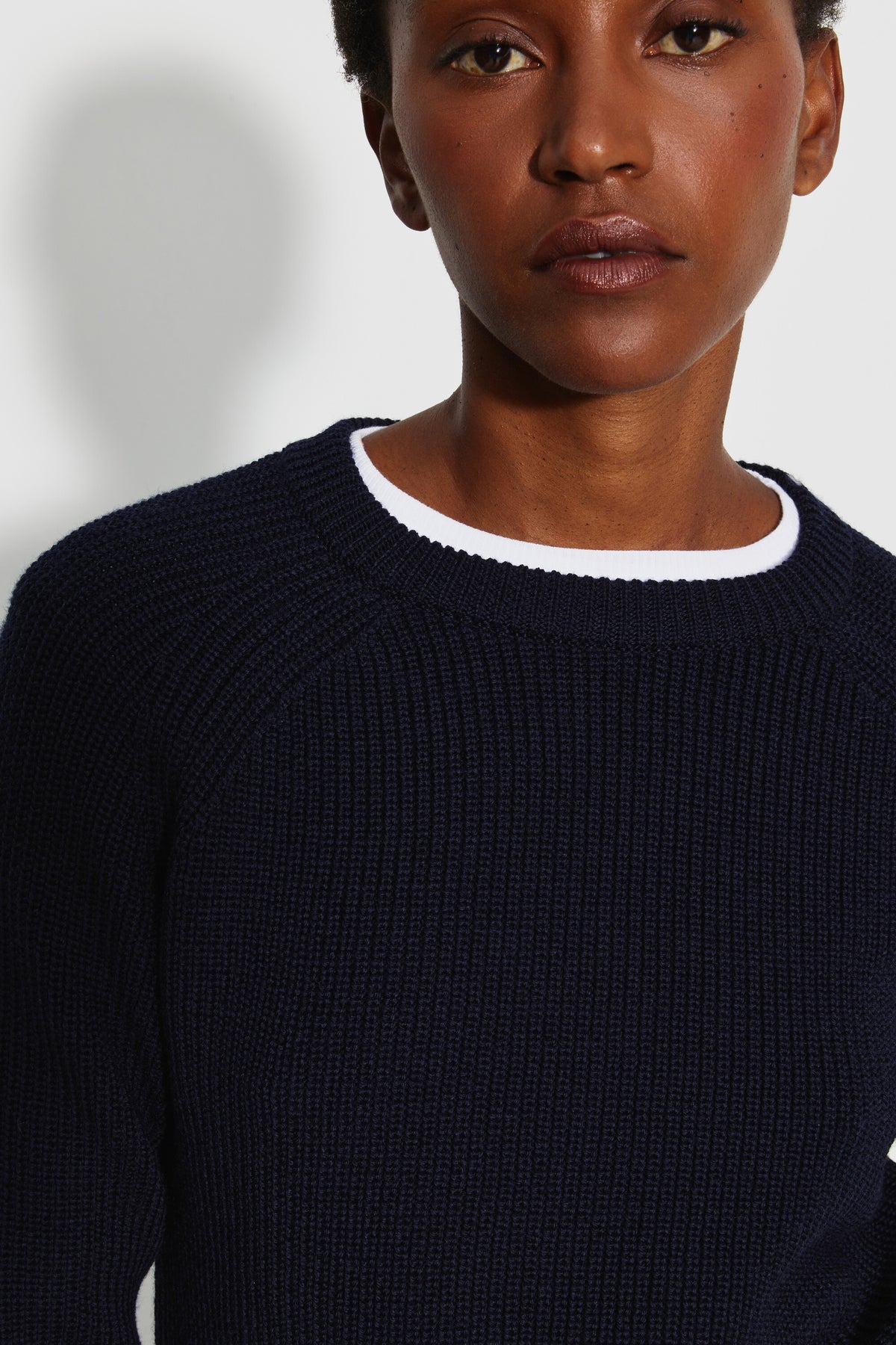 Pull femme bleu marine en laine mérinos à manches raglan, portrait rapproché montrant le col rond et la maille perlée, avec un haut blanc visible au col.