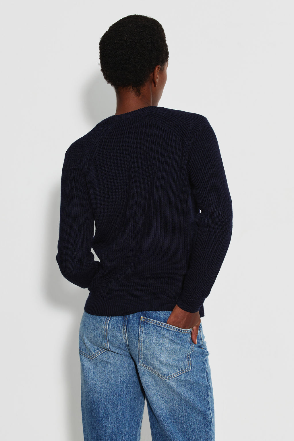 Pull femme bleu marine en laine mérinos à manches raglan, porté de dos avec un jean bleu, une main dans la poche arrière.