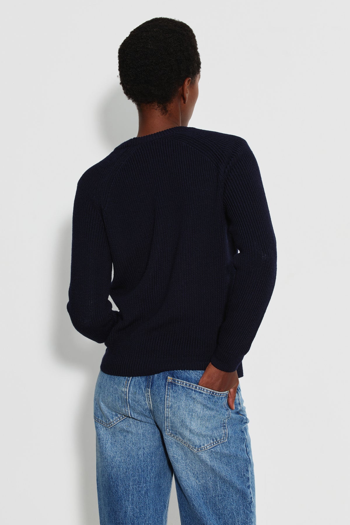 Pull femme bleu marine en laine mérinos à manches raglan, porté de dos avec un jean bleu, une main dans la poche arrière.
