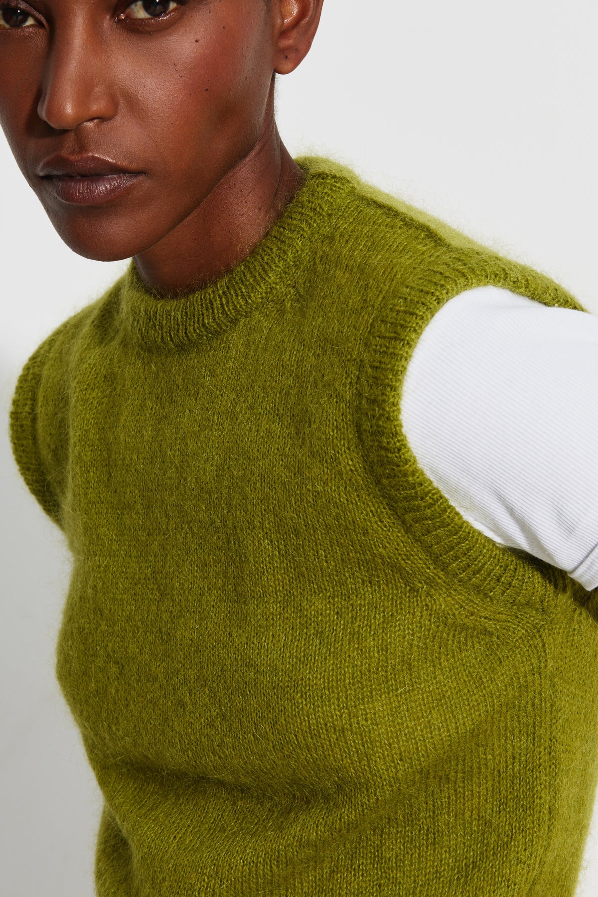 Pull mohair sans manches femme vert mousse – gros plan sur le col rond et l'emmanchure, porté sur un tee-shirt blanc.