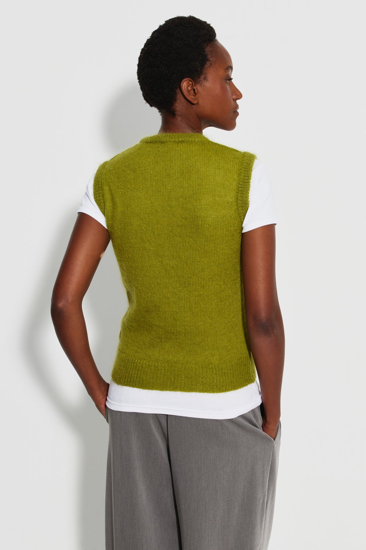 Pull mohair sans manches femme vert mousse – vue de dos, porté sur un tee-shirt blanc avec un pantalon gris.