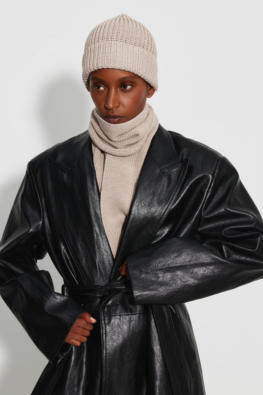 Bonnet femme beige en laine mérinos, porté avec une écharpe beige et un manteau noir brillant, vue de trois quarts.