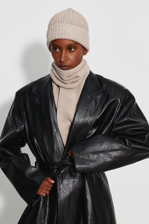 Bonnet femme beige en laine mérinos, porté avec une écharpe beige et un manteau noir brillant, vue de trois quarts.