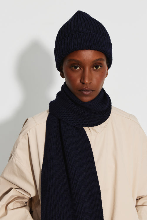 Bonnet femme bleu marine en laine mérinos, porté de face avec une écharpe assortie et une veste claire.