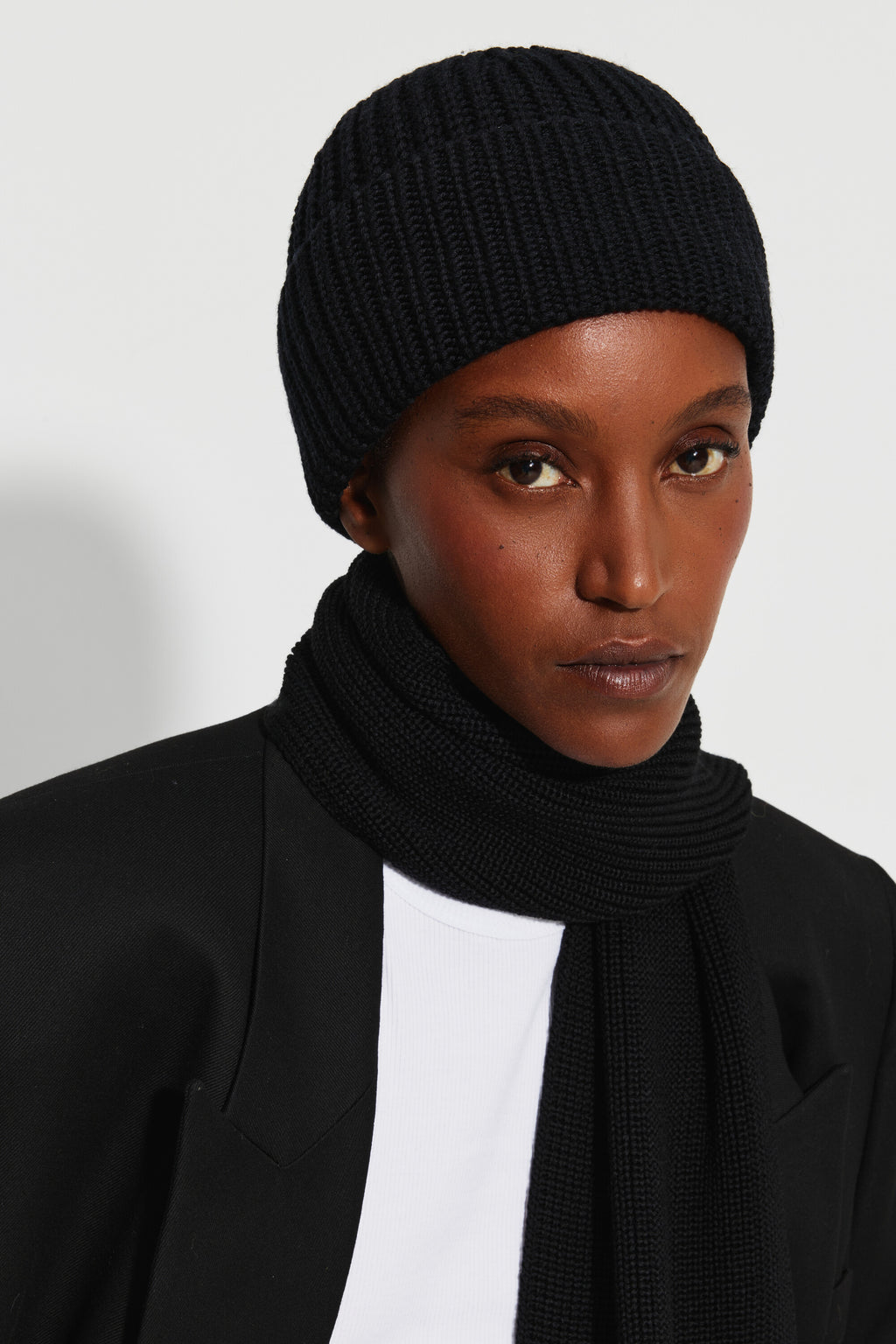 Bonnet femme noir en laine mérinos, portrait rapproché montrant la maille et le revers, avec une écharpe noire. Made in France.