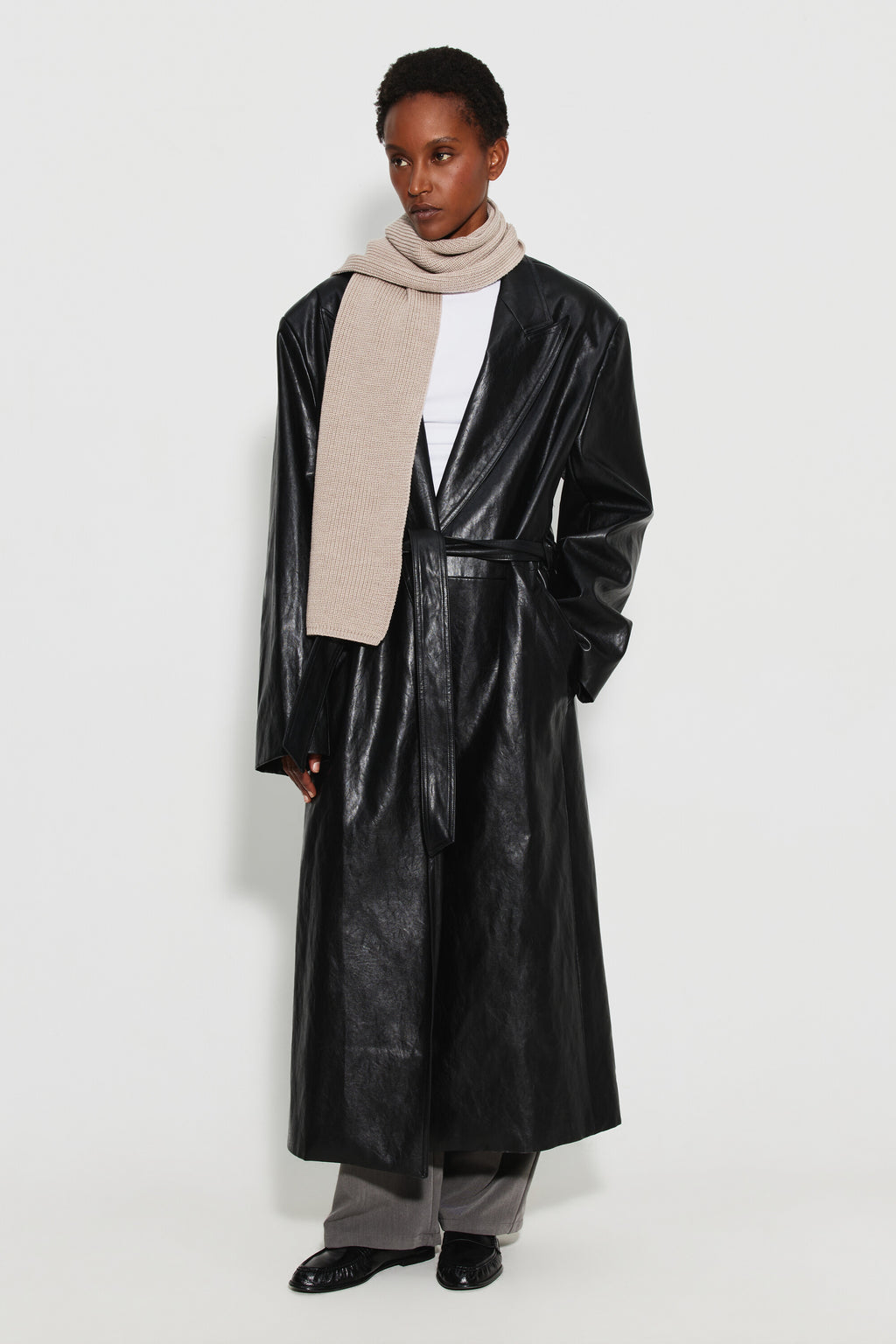 Écharpe femme beige en laine mérinos, portée autour du cou avec un long manteau noir brillant, vue en pied.