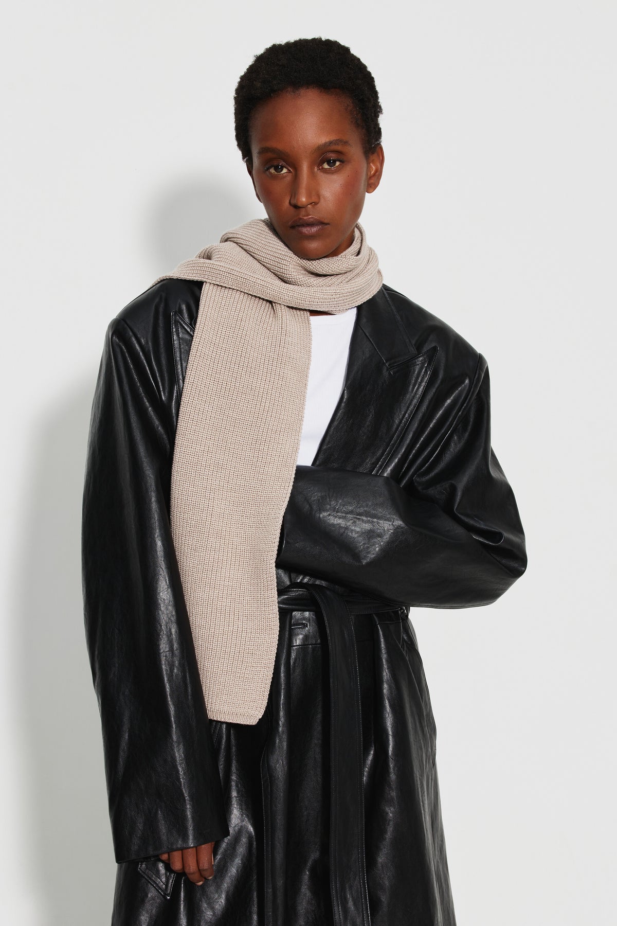 Écharpe femme beige en laine mérinos, portée enroulée autour du cou avec un pan sur la poitrine et un manteau noir brillant. Made in France.