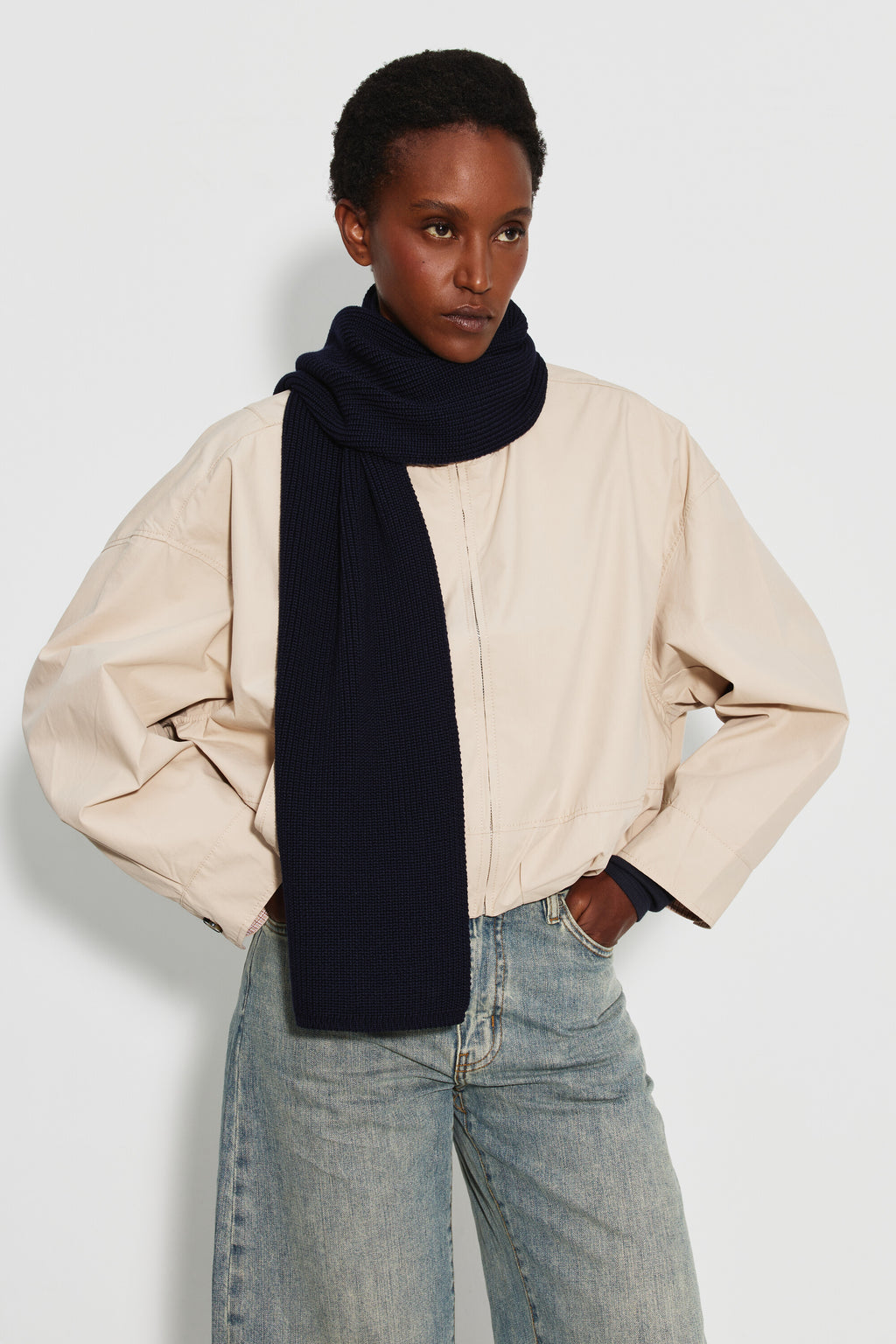 Écharpe femme bleu marine en laine mérinos, portée enroulée autour du cou avec un pan sur la poitrine, une veste claire et un jean clair. Made in France.