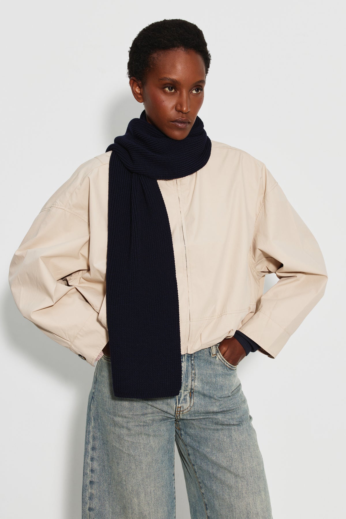 Écharpe femme bleu marine en laine mérinos, portée enroulée autour du cou avec un pan sur la poitrine, une veste claire et un jean clair. Made in France.
