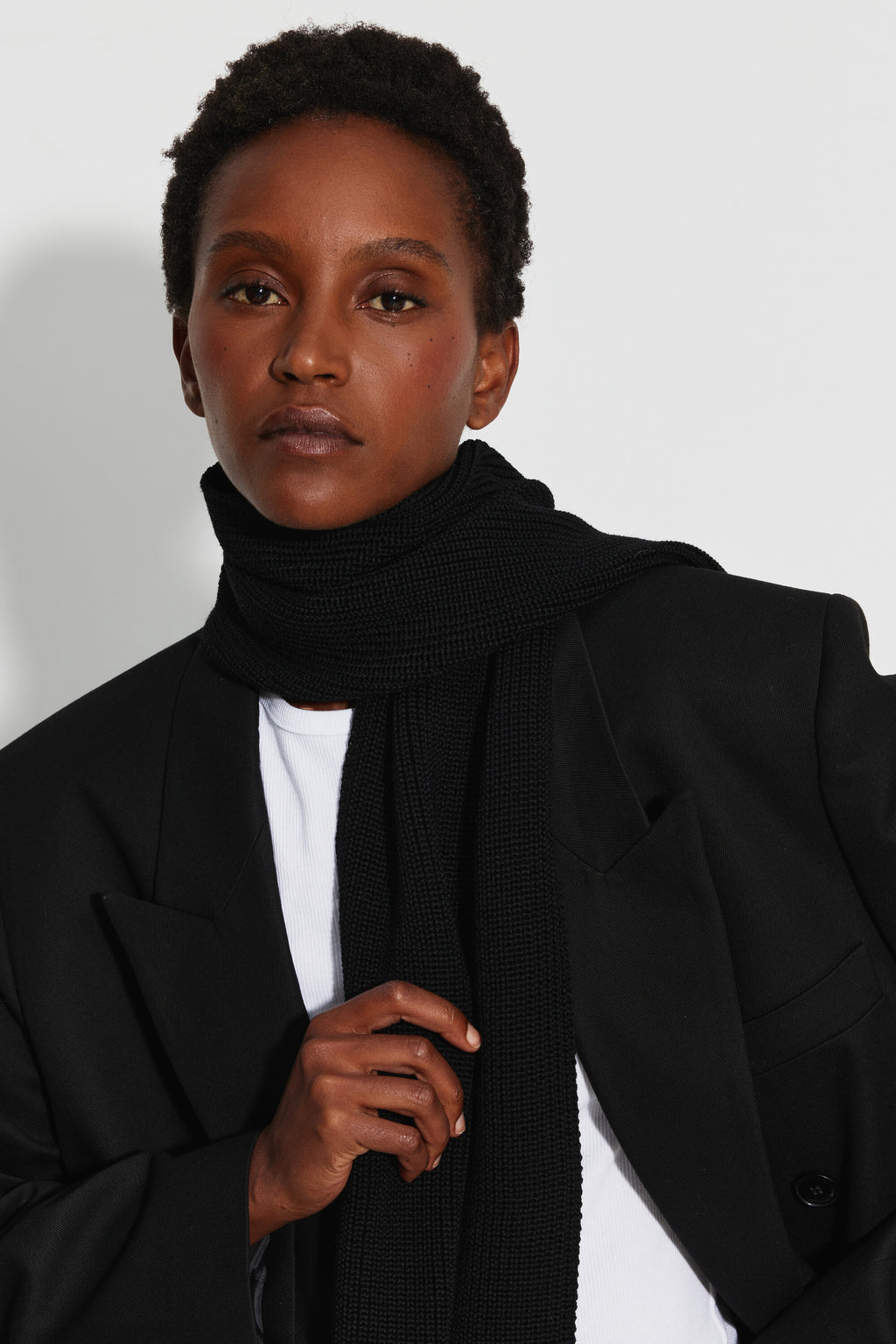 Écharpe femme noire en laine mérinos, portrait rapproché montrant l’écharpe autour du cou, une main tenant son extrémité.