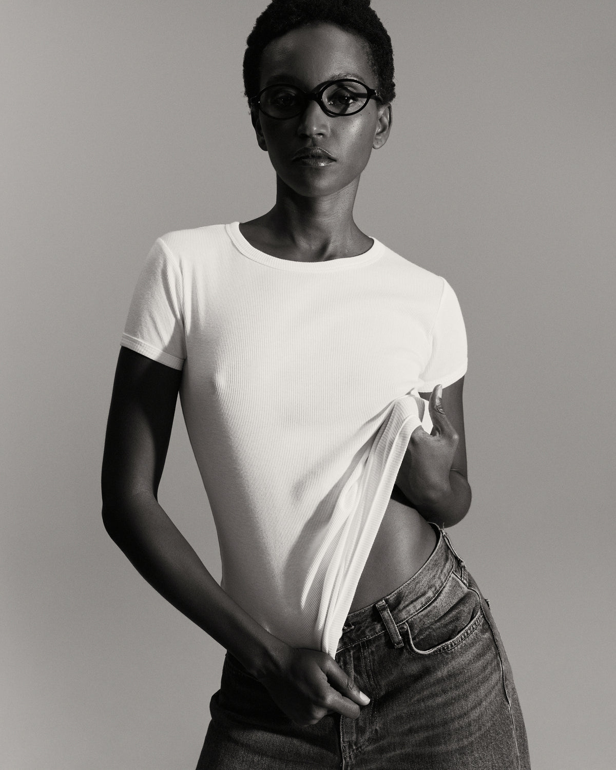 Maillot de corps femme blanc à manches courtes, modèle soulevant légèrement le bas du vêtement, photo en noir et blanc.