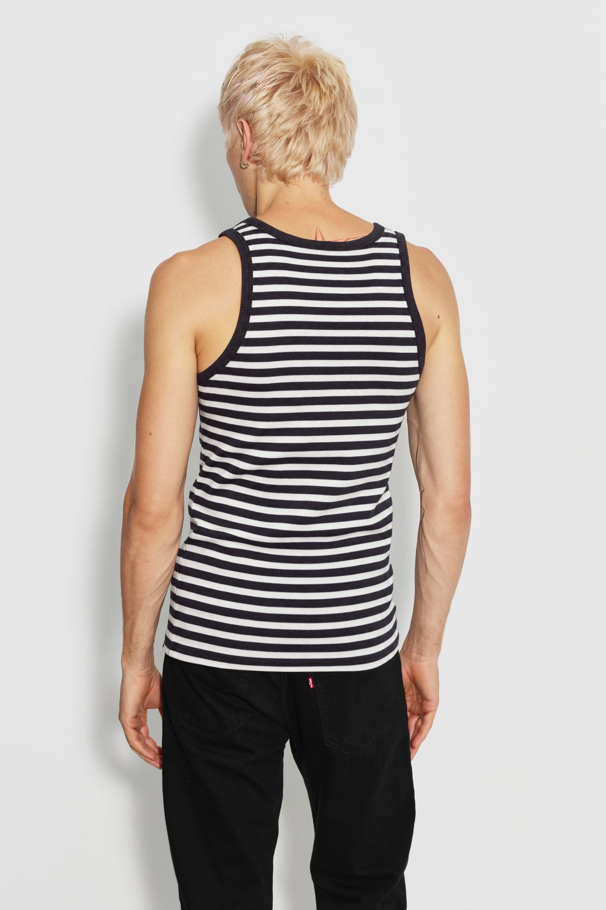 Débardeur homme rayé noir et écru en coton bio côtelé, porté de dos avec un pantalon noir, vue des rayures et du dos nageur.