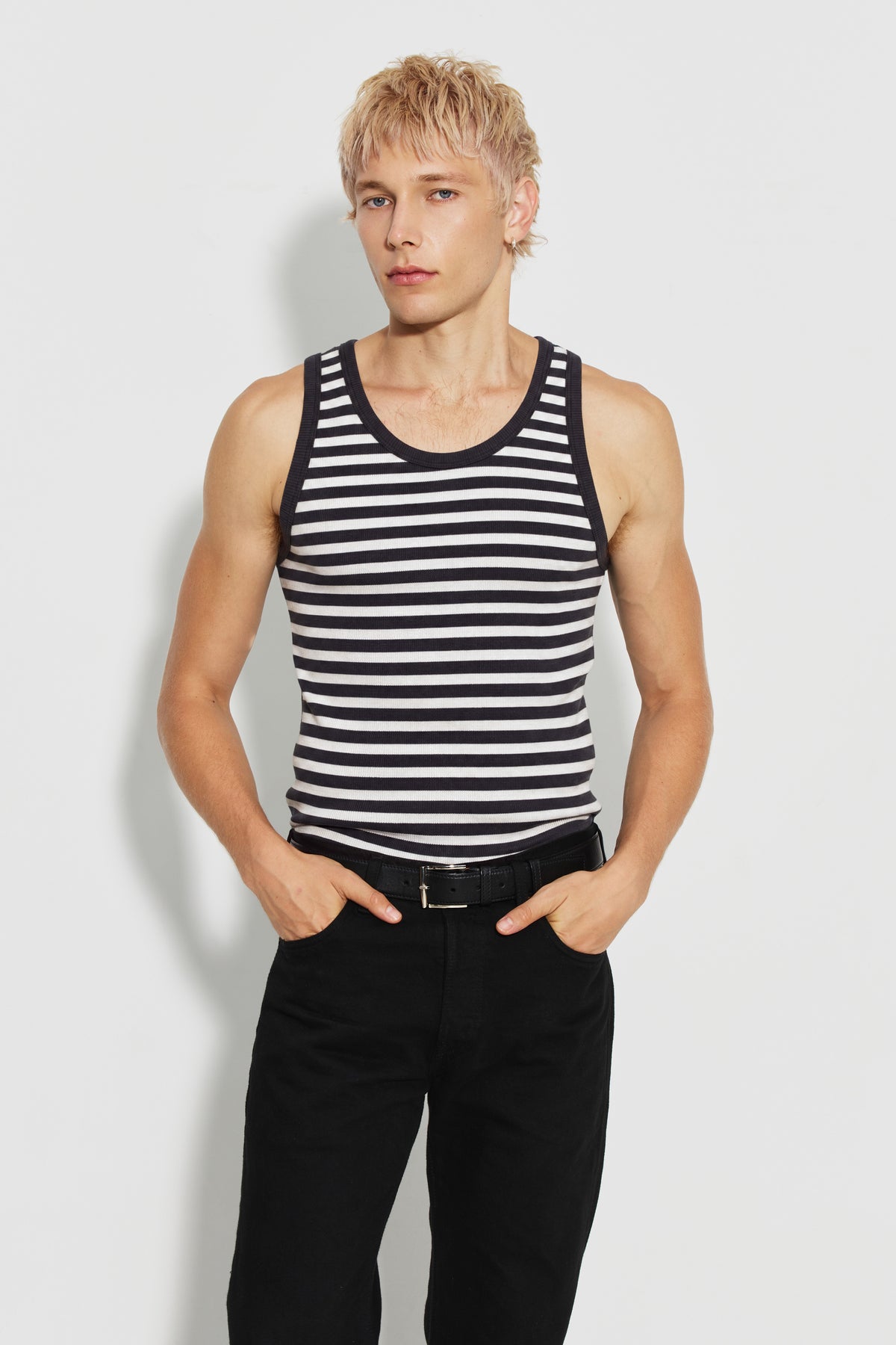 Débardeur homme rayé noir et écru en coton bio côtelé, porté de face avec un pantalon noir, les mains dans les poches. Made in France.
