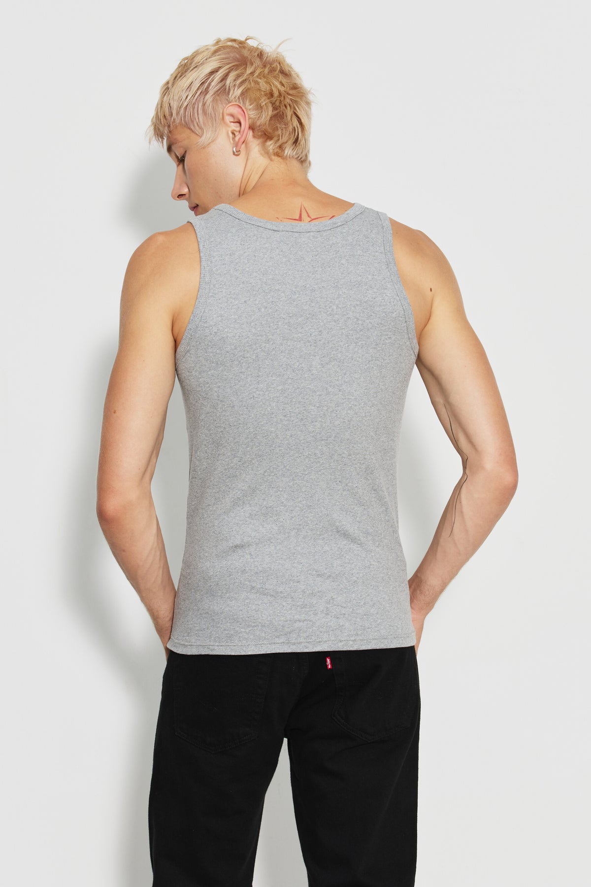 Débardeur Marcel Signature gris chiné homme en coton Pima côtelé, porté de dos avec un pantalon noir, la tête tournée sur le côté.