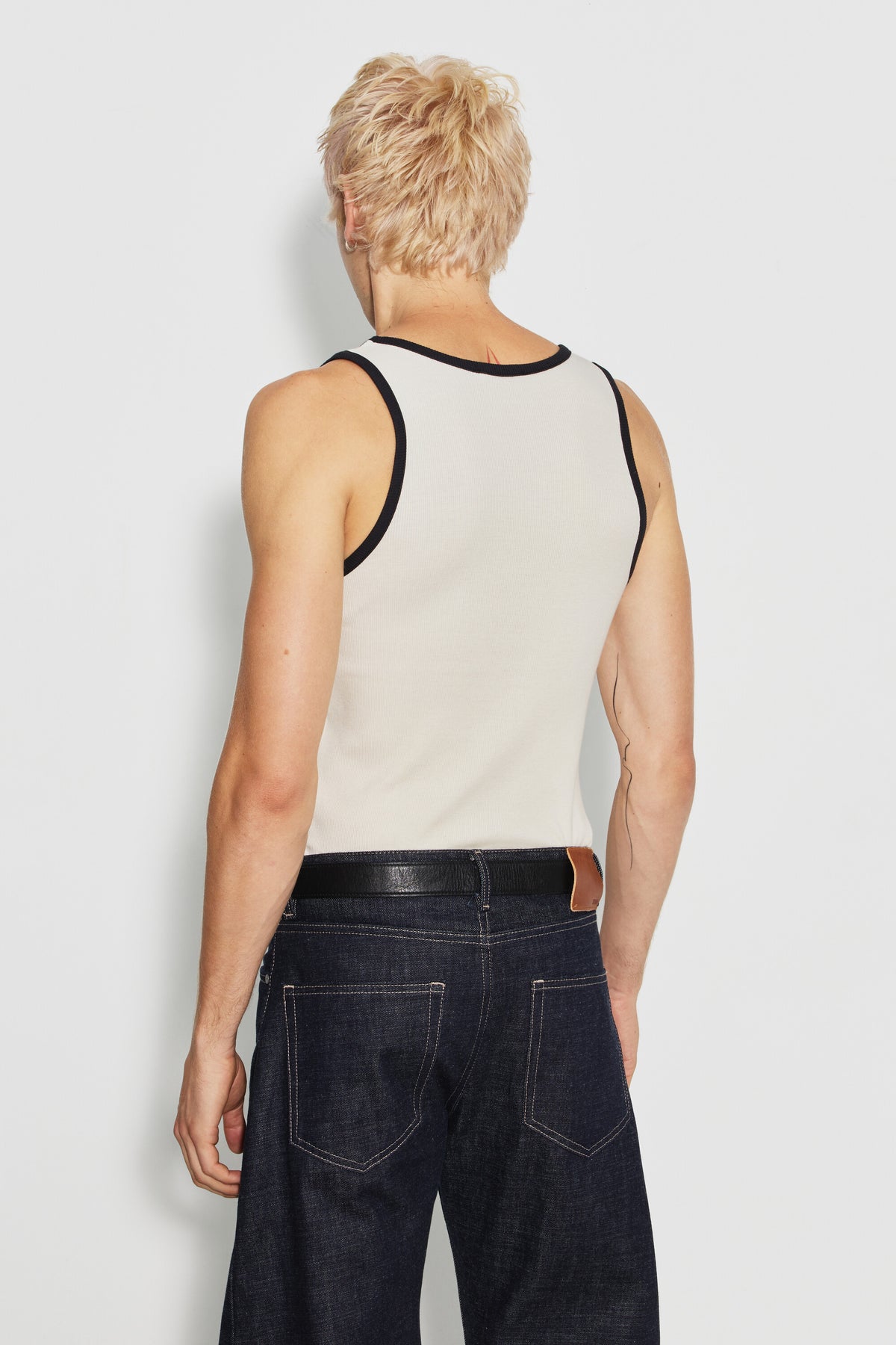 Débardeur homme écru et noir en coton Pima côtelé, porté de dos avec un jean foncé et une ceinture noire.
