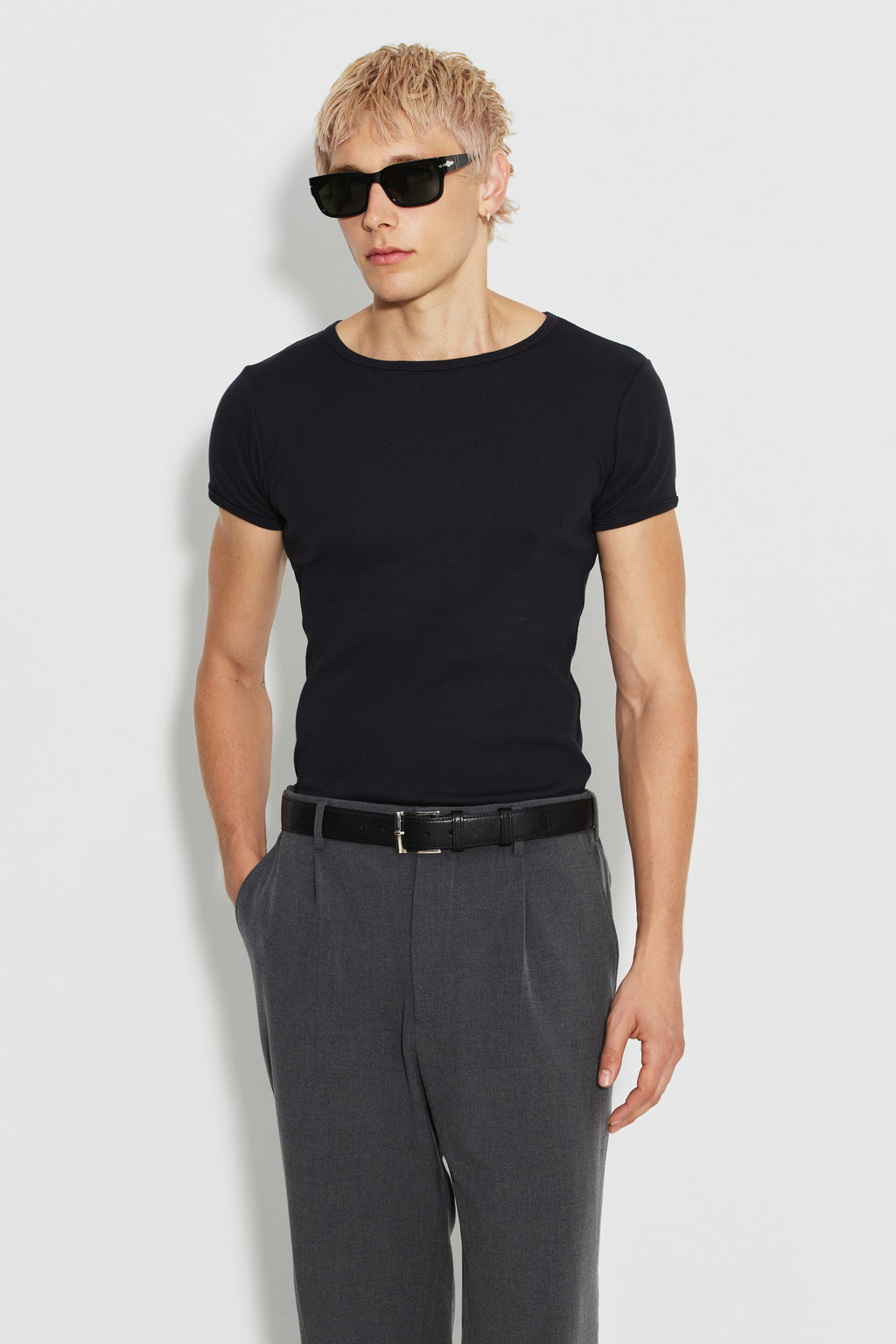 Maillot de corps homme noir à manches courtes en coton Pima côtelé, porté de face avec un pantalon gris, une main dans la poche. Made in France.
