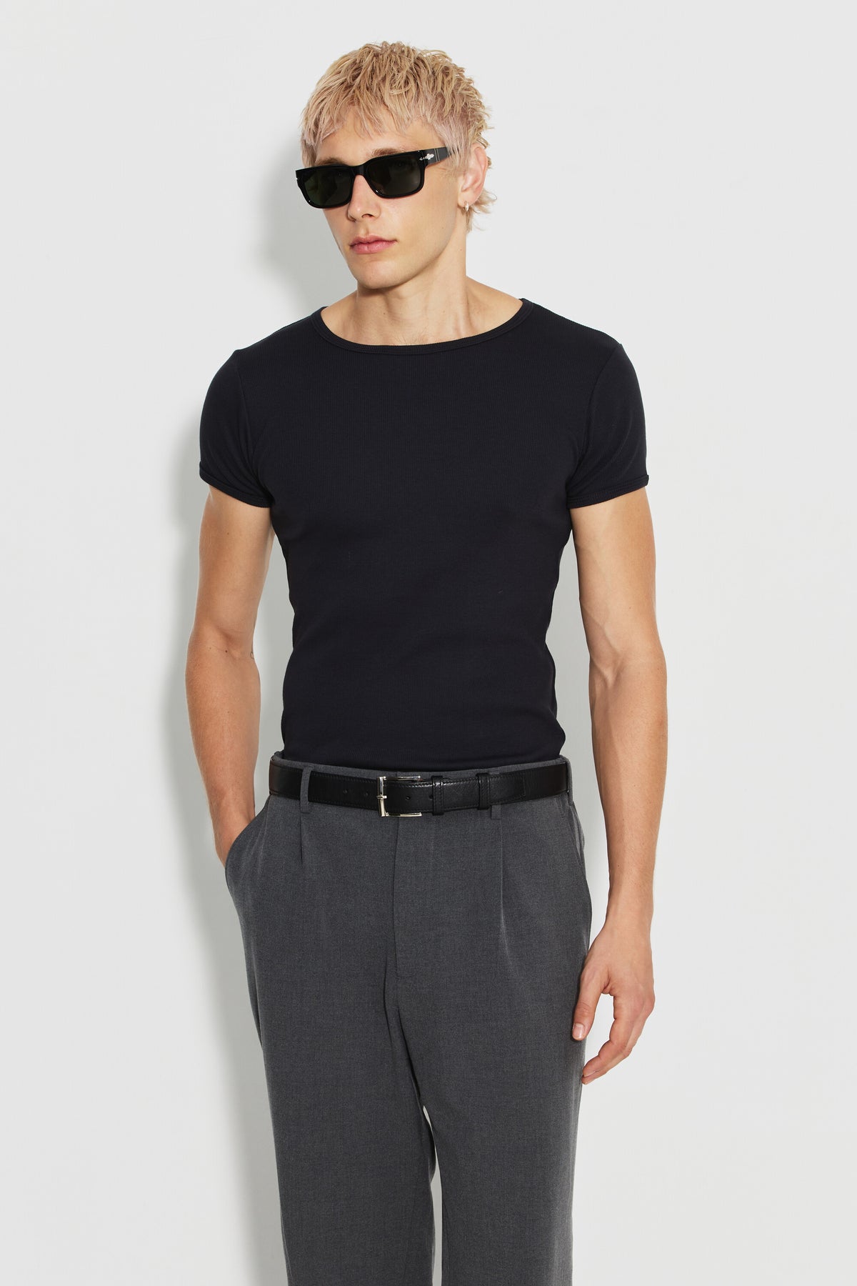 Maillot de corps homme noir à manches courtes en coton Pima côtelé, porté de face avec un pantalon gris, une main dans la poche. Made in France.