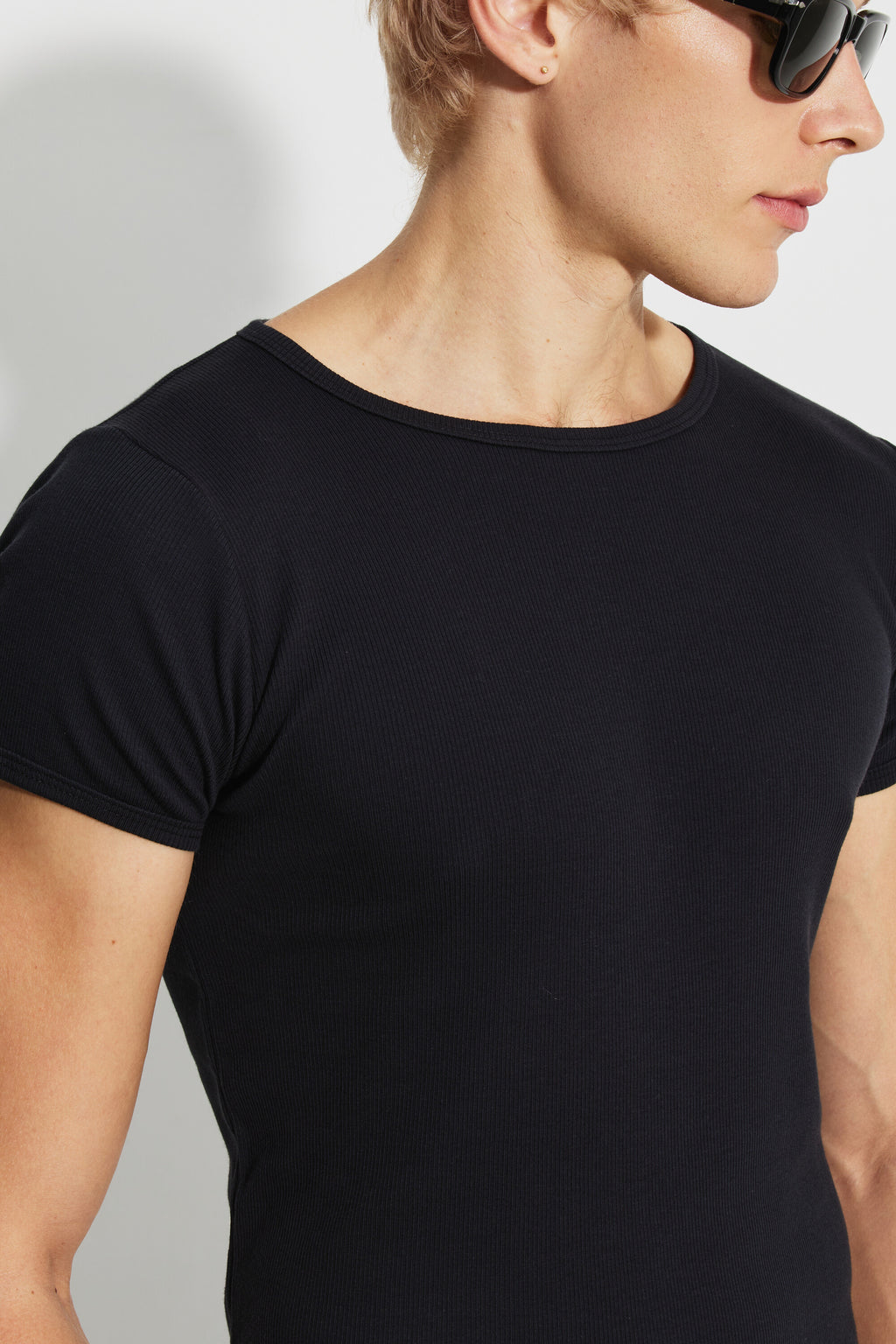 Maillot de corps homme noir à manches courtes en coton Pima côtelé, vue rapprochée du col rond et de l’épaule, avec des lunettes de soleil.